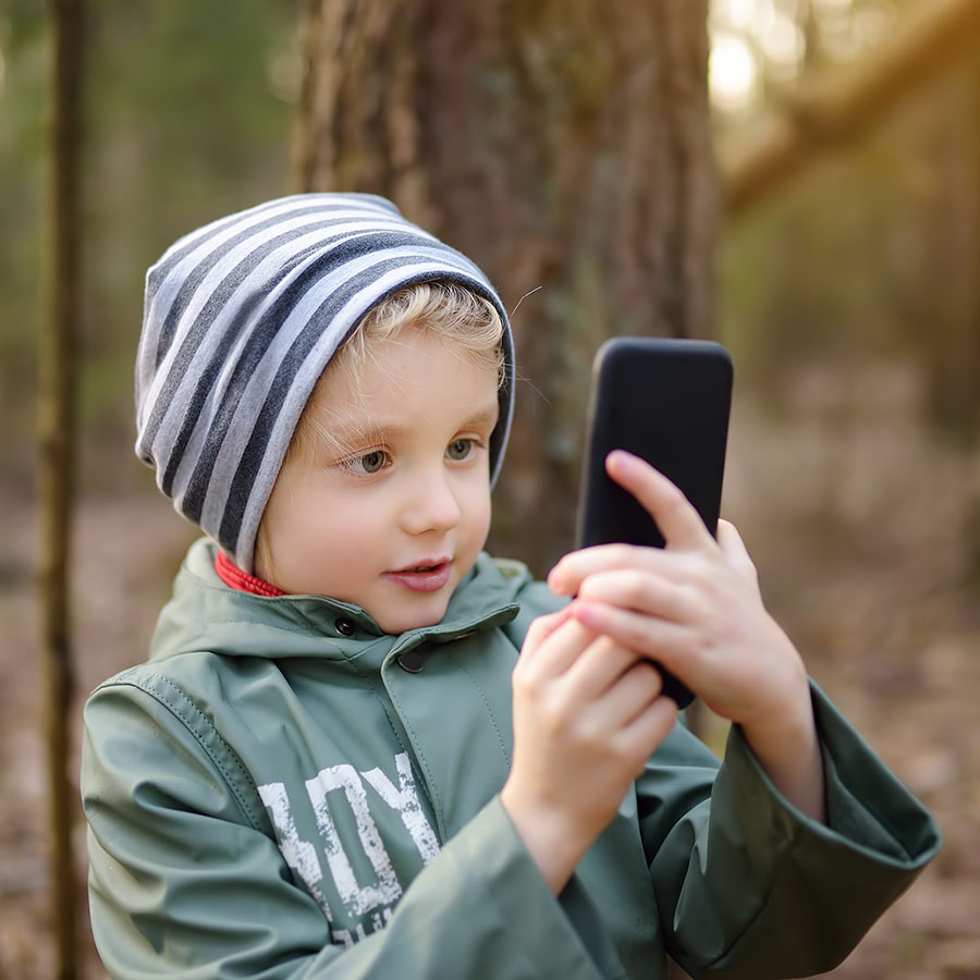 Little boy making a call on smartphone in the forest