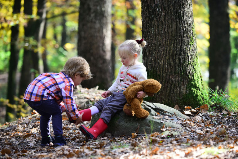 Little boy in forest helping his sister put her boots on